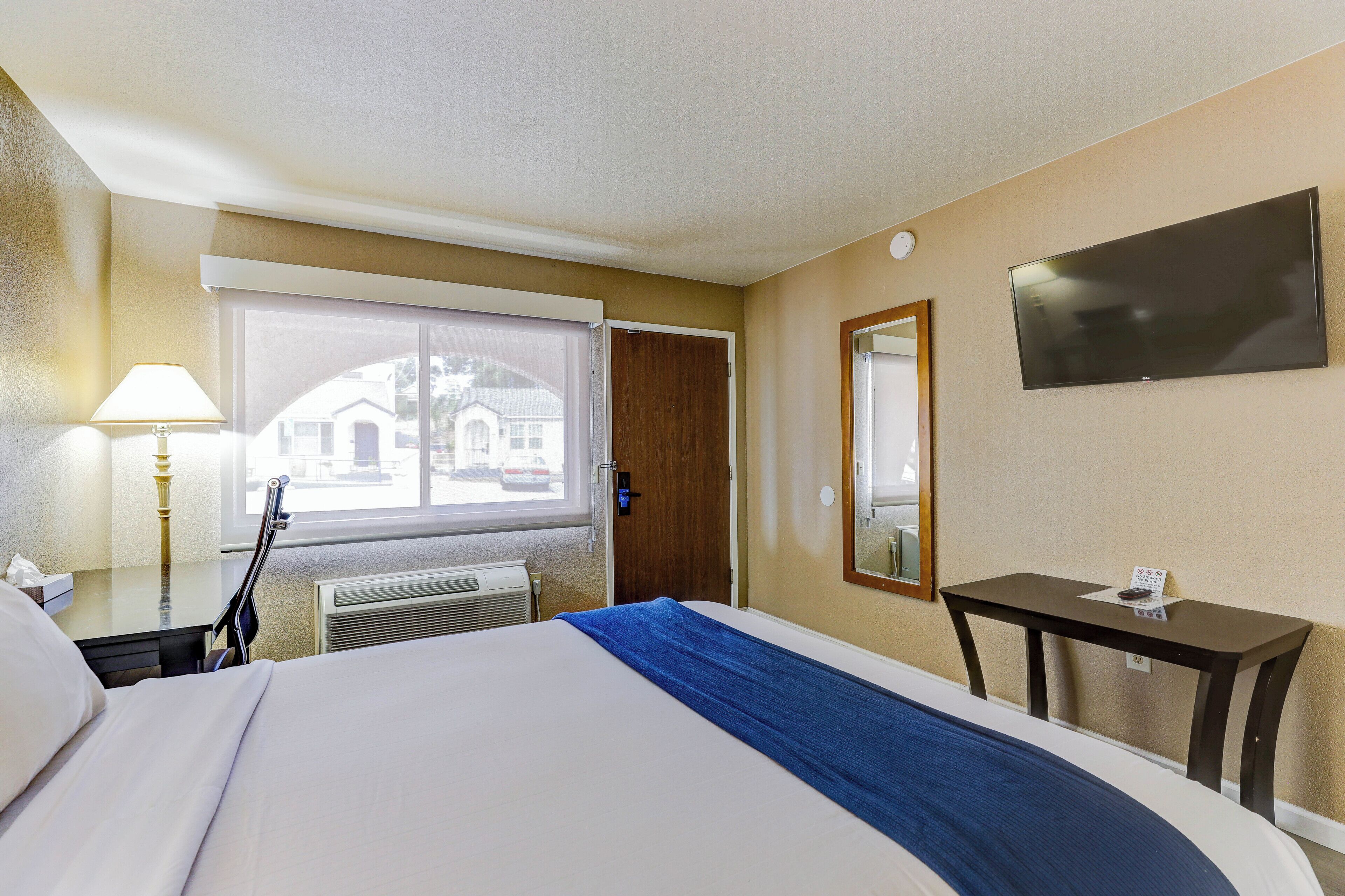 A hotel room with a bed, a desk, a chair, a TV, a window, and a door.