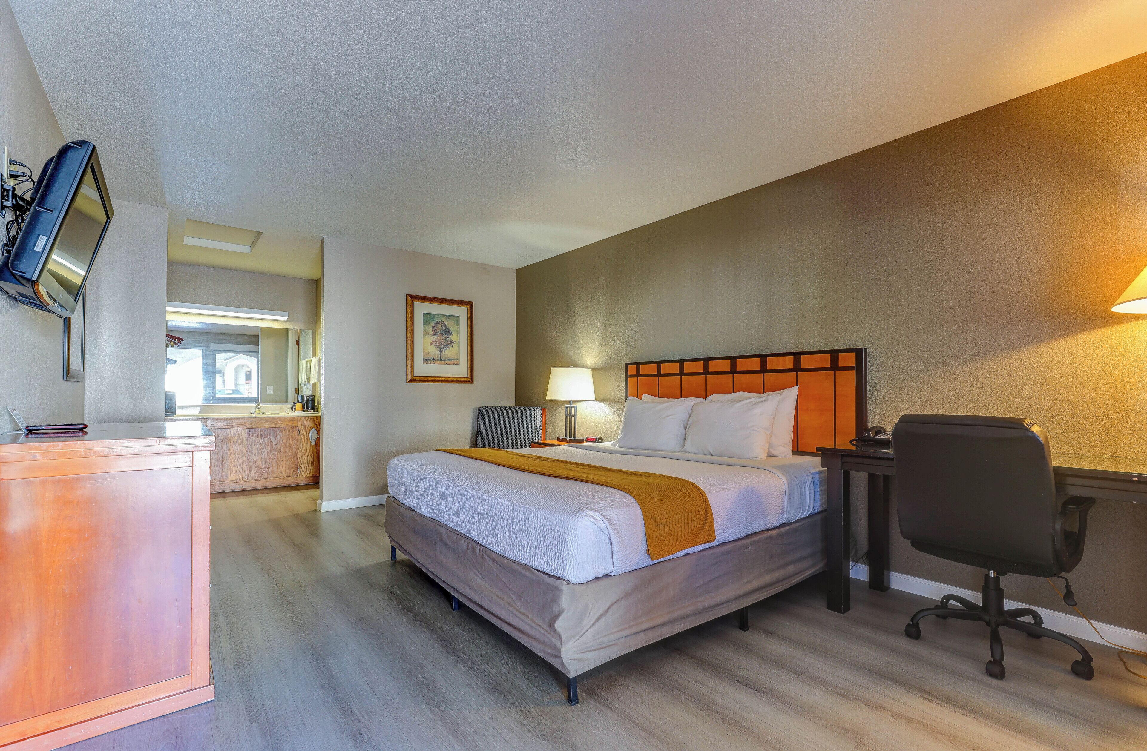 Habitación de hotel con cama, mesita de noche, lámpara, silla y televisor montado en la pared.