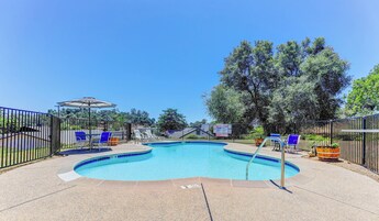 Una piscina de borde curvo, rodeada por una valla, con sillas de descanso y una zona cubierta.