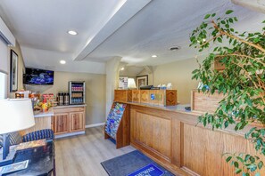 A reception area with a wooden counter, a digital screen, a coffee station, and a plant. - Rodeway Inn Jackson - Martell (Jackson)