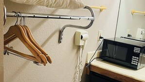 Habitación de hotel pequeña con cama, un escritorio con microondas, perchero y maleta negra en el suelo.