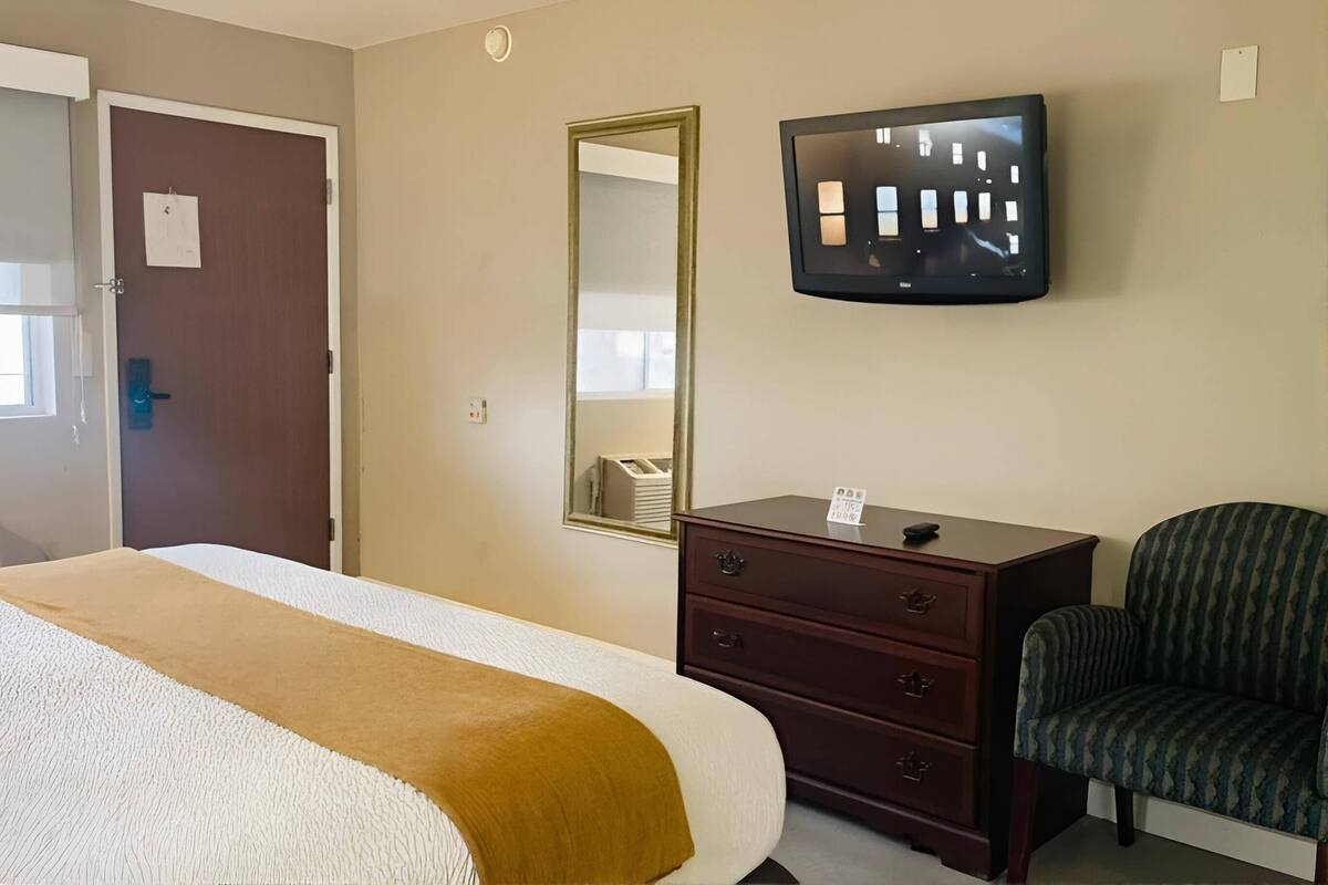 A hotel room with a bed, a dresser, a chair, a television, and a mirror.