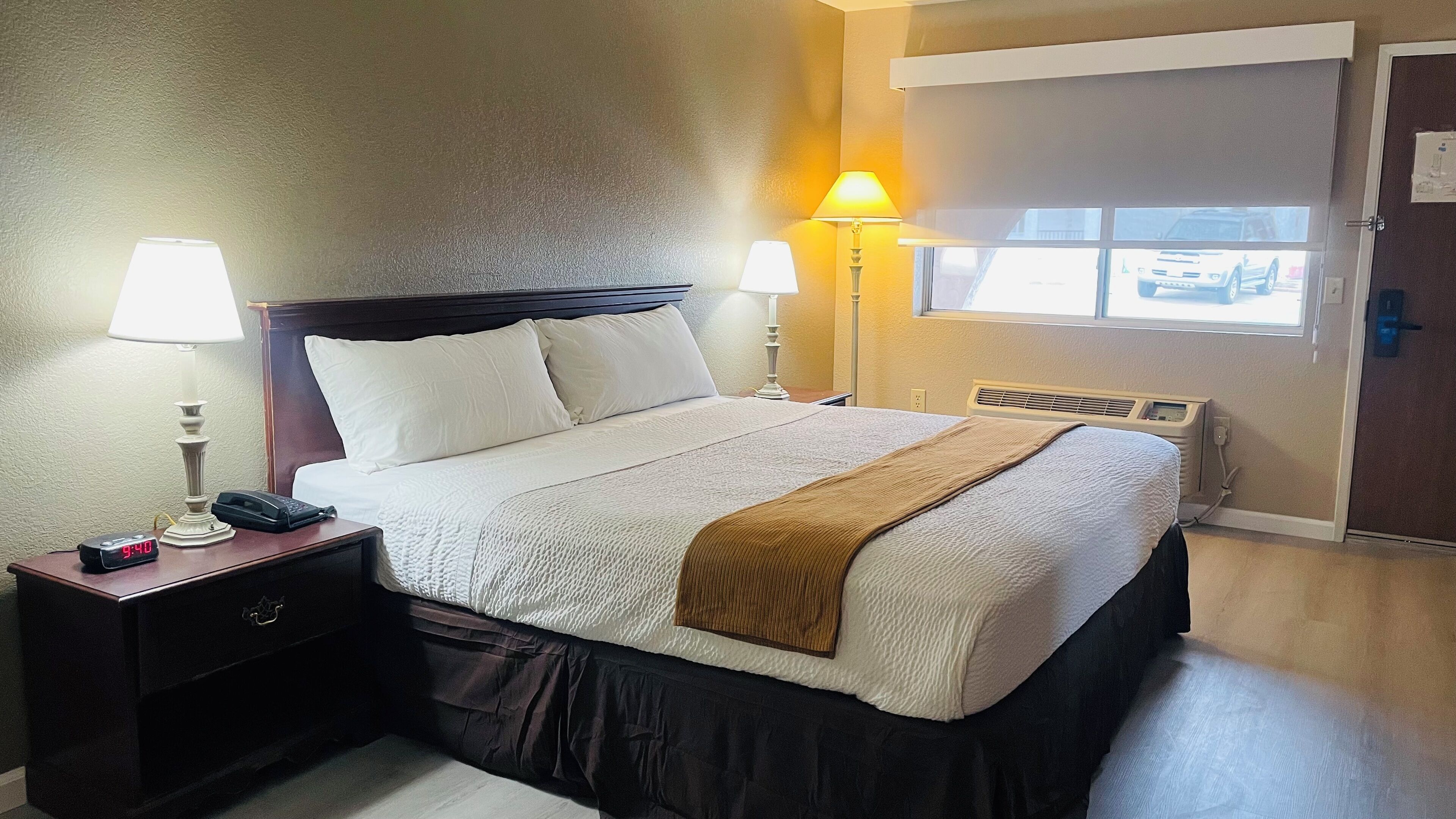 A hotel room with a bed, two bedside lamps, a nightstand with a phone, and a window with a view of the outside.