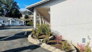 Un edificio con fachada blanca, un porche cubierto y un estacionamiento con algunos vehículos.