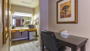Habitación de hotel con escritorio, silla, microondas y un cuadro en la pared.
