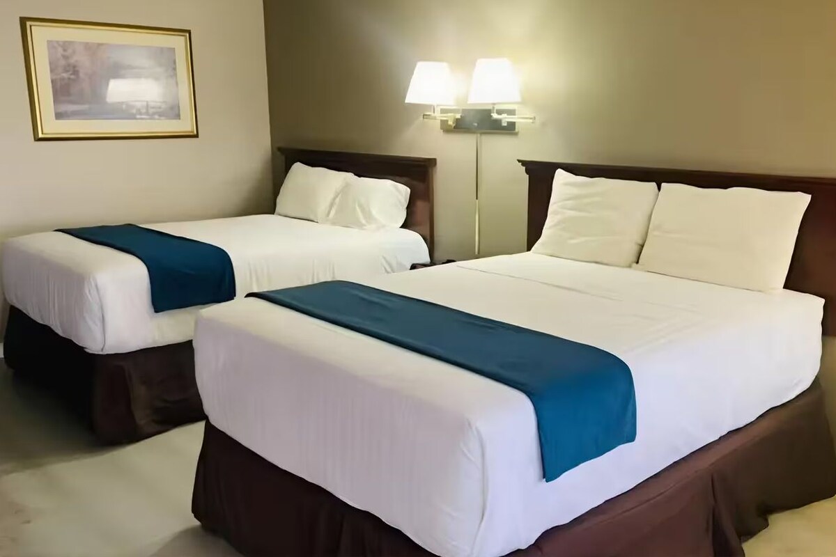 Two single beds with white linens and blue throw blankets, a wall-mounted lamp, and a framed picture on the wall.