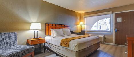 A hotel room with a bed, bedside table, chair, and a window with a view.