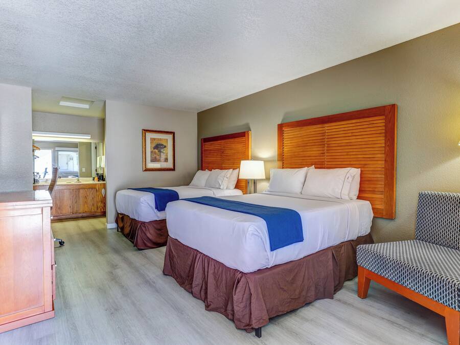 Quarto de hotel com duas camas, uma escrivaninha, uma cadeira e um quadro na parede.