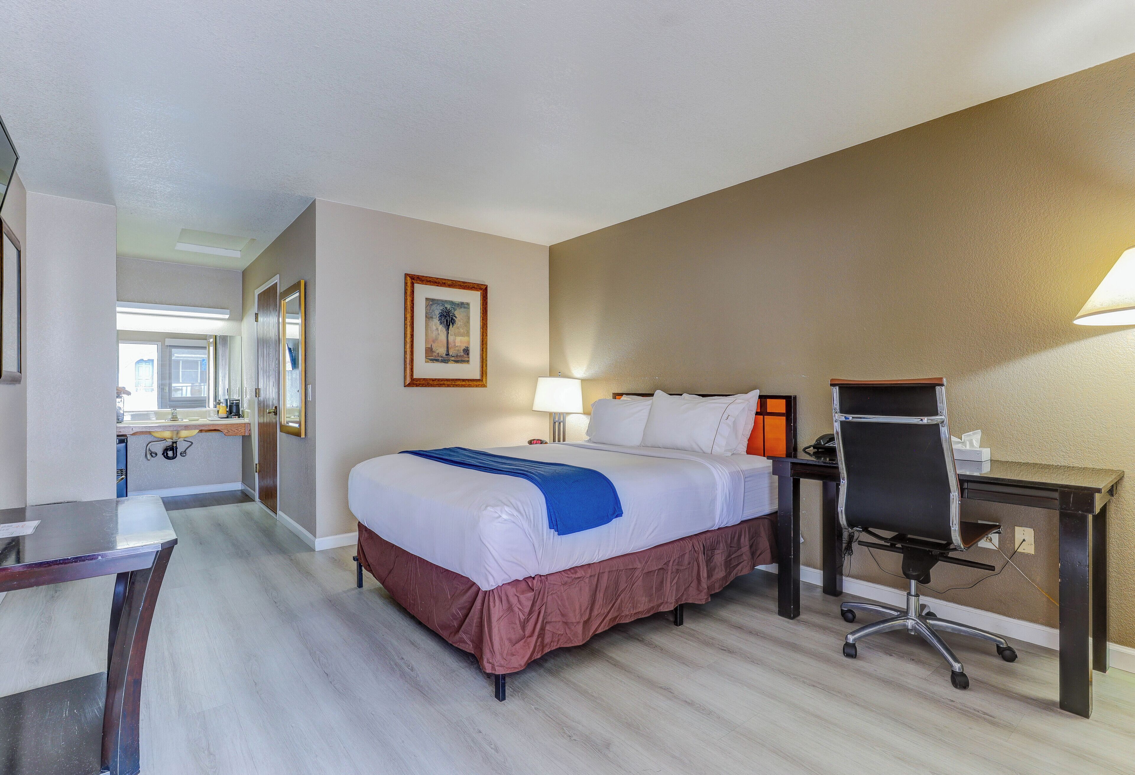 A hotel room with a bed, desk, chair, and a bathroom visible through an open door.