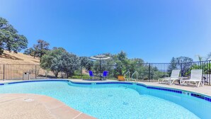 Una piscina cristalina con borde de azulejos azules, rodeada por una valla y un área techada con sillas y una mesa.