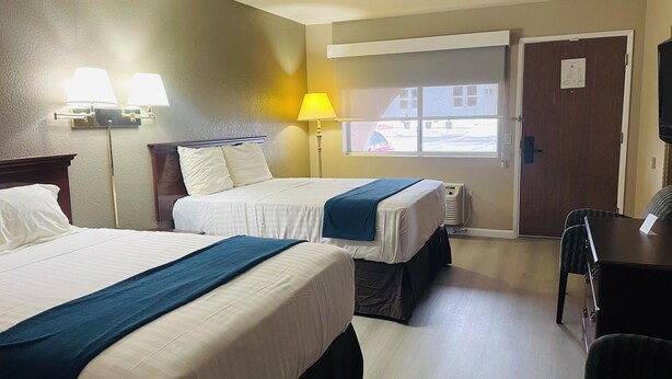 Habitación de hotel con dos camas, un escritorio, una silla, una lámpara y una ventana con vistas al exterior.