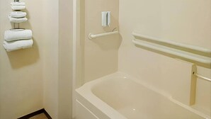 A bathroom with a bathtub, a towel rack with folded towels, and a handrail.