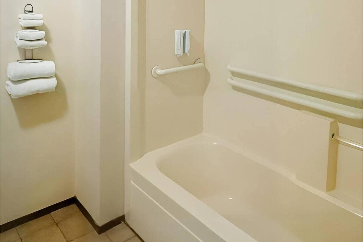 A bathroom with a bathtub, a towel rack with folded towels, and a handrail.