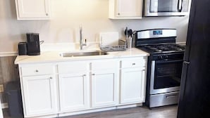 A kitchen with white cabinets, a stainless steel microwave, a stove, and a black refrigerator.