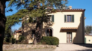 A two-story building with a stone wall in front, a large tree, and a clear blue sky. - Self-contained apartment with independent access in Farmhouse. (Toscana)