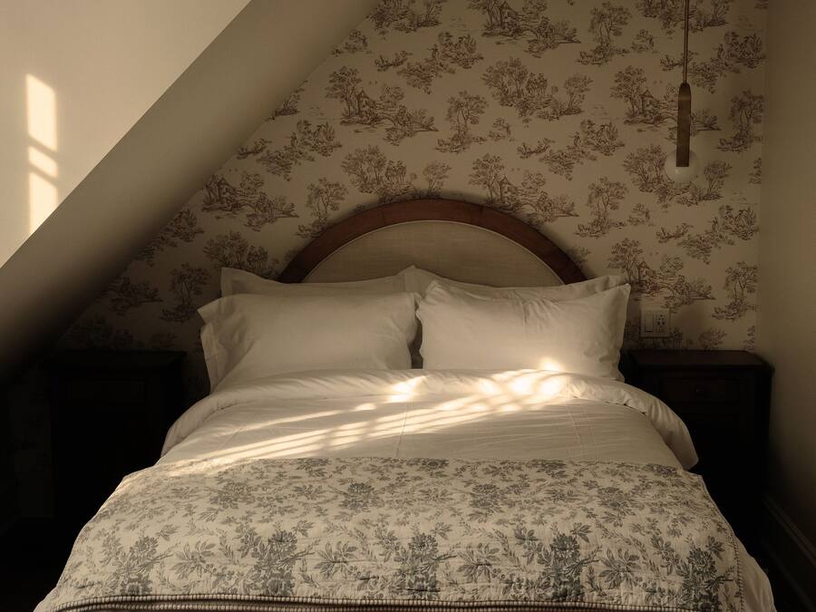 A bedroom with a sloped ceiling, a wooden headboard, a bed with floral bedding, and a hanging light fixture.
