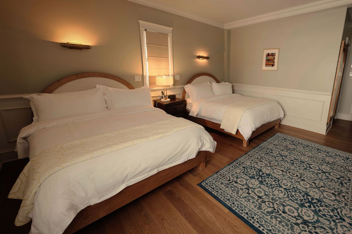Une chambre d’hôtel avec deux lits, un plancher en bois, un tapis à motifs et des lampes fixées au mur.