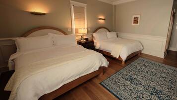 Habitación de hotel con dos camas, piso de madera, alfombra estampada y lámparas fijadas a la pared.