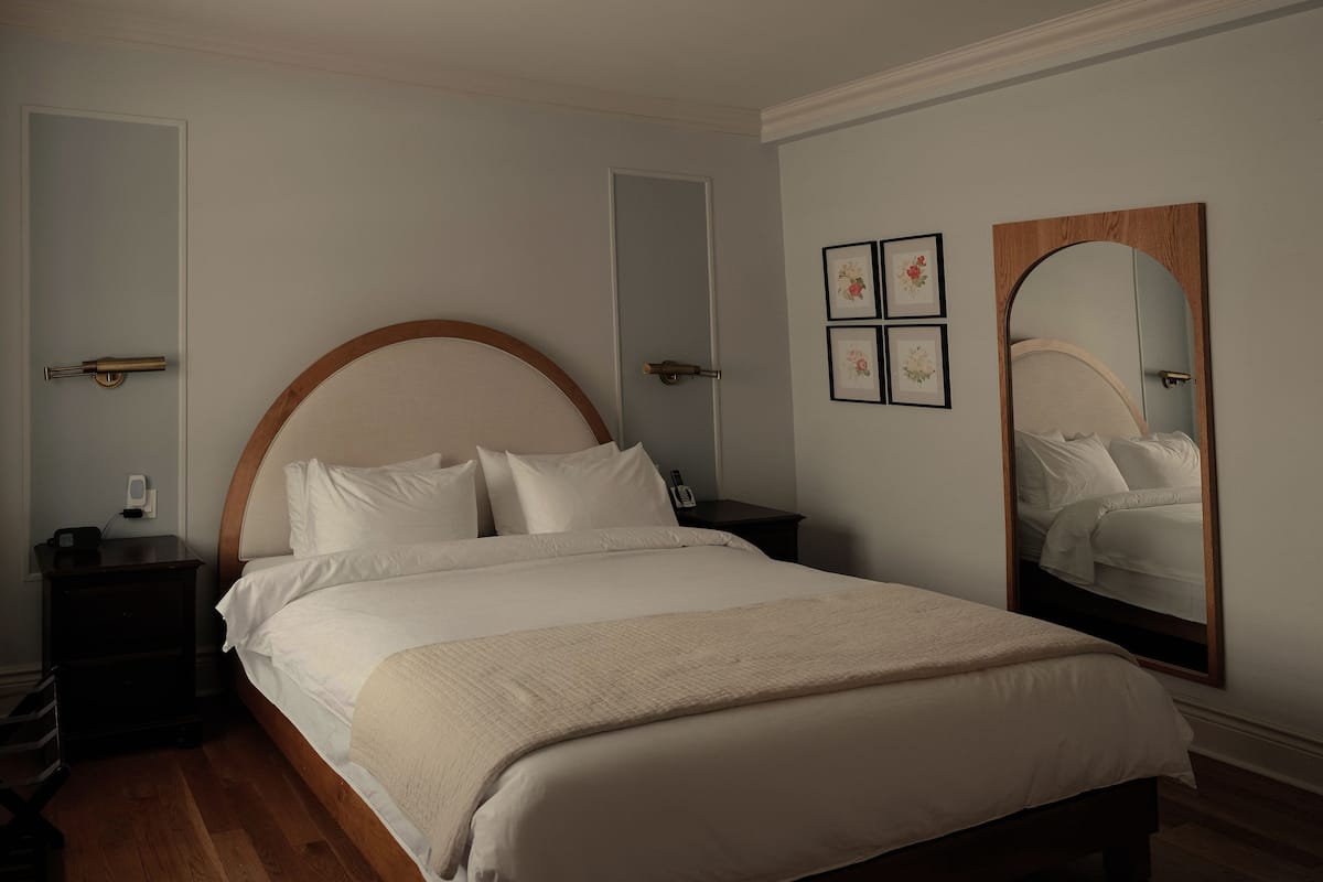 Une chambre à coucher bien rangée, avec un grand lit, une table de chevet, une commode et un miroir fixé au mur.