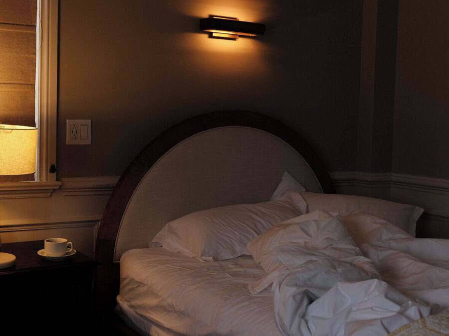 Un dormitorio con una cama, una mesita de noche con una taza y una lámpara de pared.