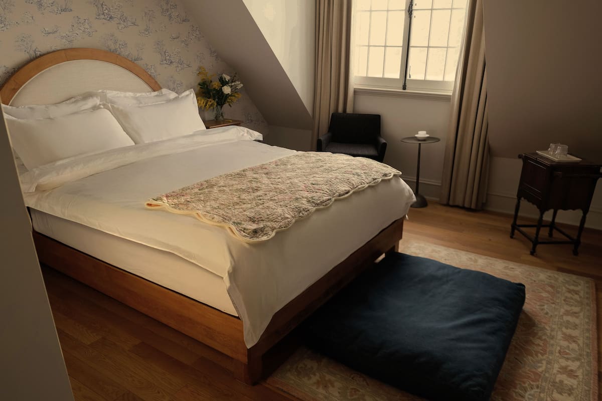 Une chambre avec un grand lit, une petite table, une chaise et une fenêtre avec des rideaux.