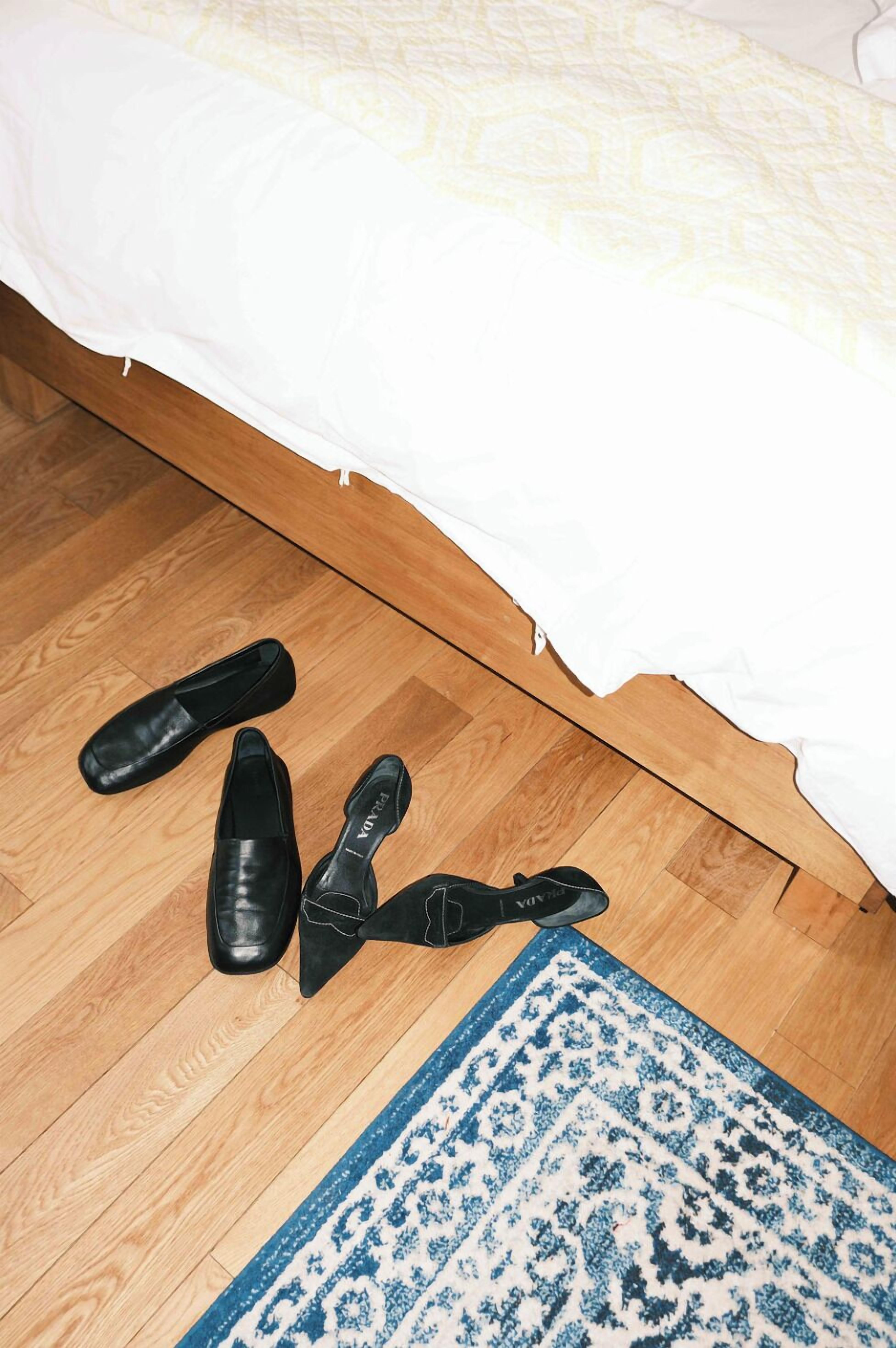 A bedroom with a wooden floor, a white bedspread, and a blue patterned rug.