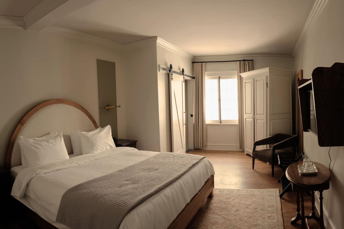 Une chambre avec un grand lit, un bureau, une chaise, une armoire et une fenêtre.