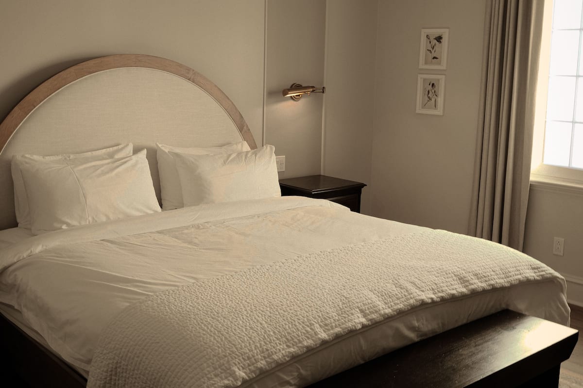 Un lit bien fait, avec une tête de lit en bois, une table de chevet et un luminaire fixé au mur.