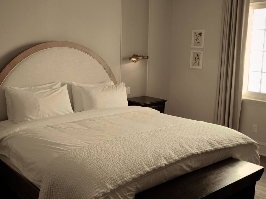 A neatly made bed with a wooden headboard, a bedside table, and a wall-mounted light fixture.