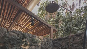 A stone-walled outdoor shower area with a circular seating area and two small shelves with bottles. - Hotel Ambil (Barichara)