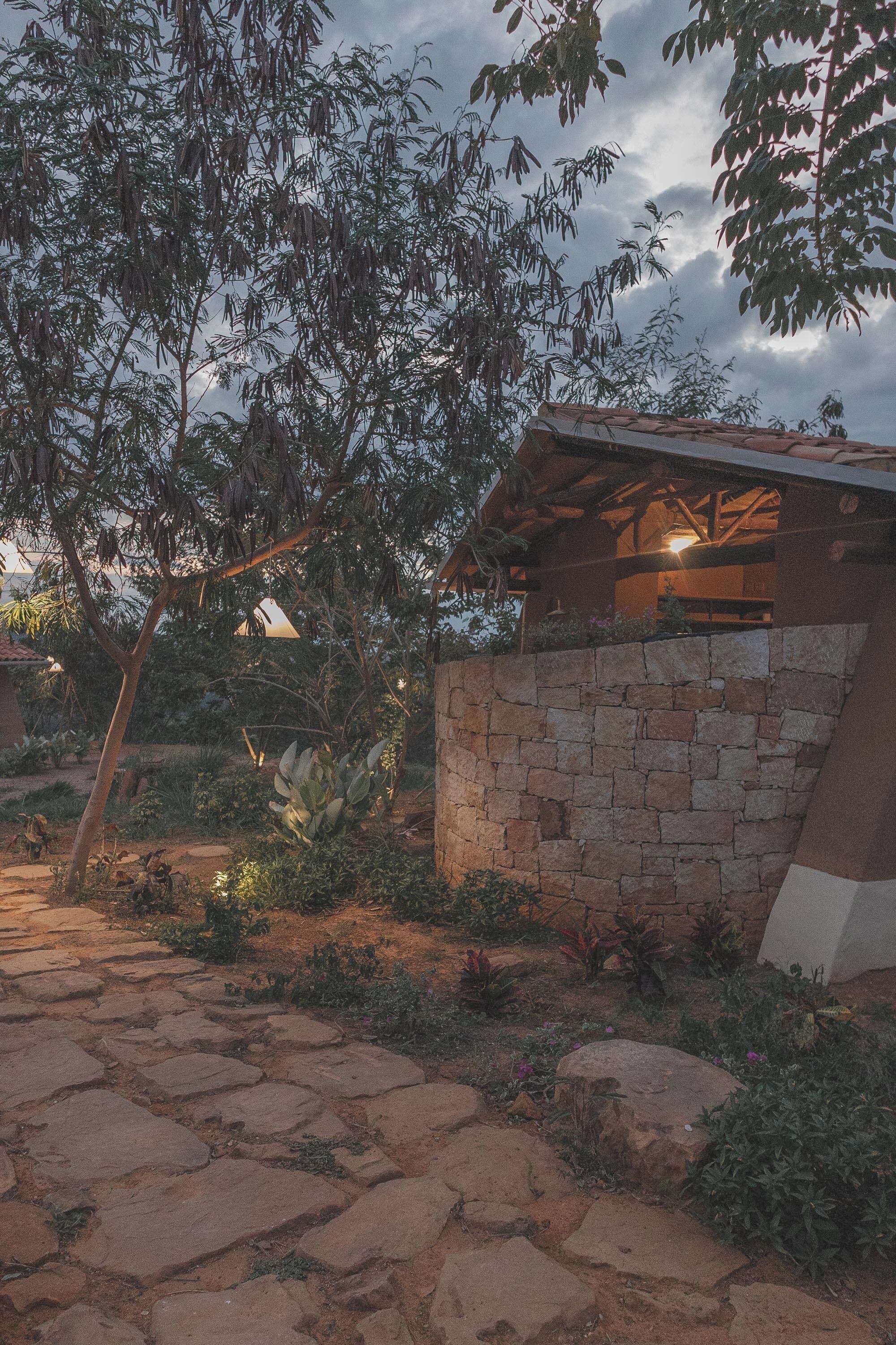 Un espace extérieur rustique agrémenté d’un mur en pierre, d’une pergola en bois et d’un sentier.