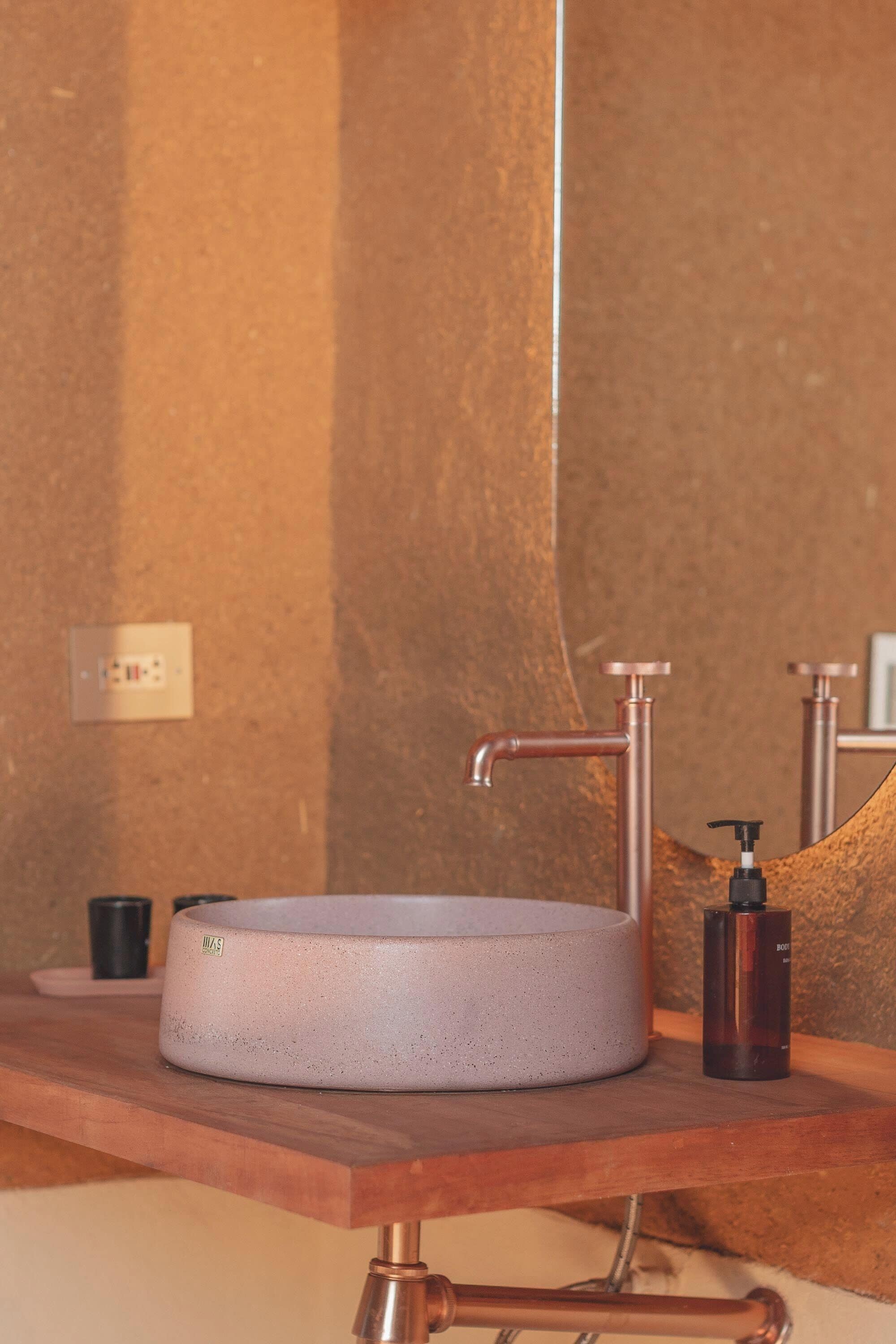 A bathroom sink with a round basin, a faucet, and a soap dispenser on a wooden countertop.