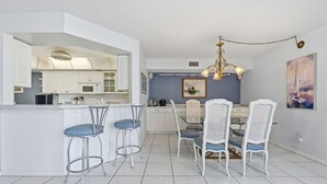 Eine moderne Küche mit weißen Schränken, einer zentralen Kochinsel mit Barhocker und einem Essbereich mit einer Chandelüster.