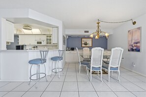 A modern kitchen with white cabinets, a central island with bar stools, and a dining area with a chandelier. - Waterfront Retreat in St. Petersburg – Spacious 2-BR Condo with Balcony & Pool (Isla Del Sol)