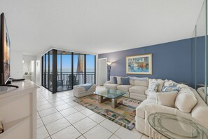 Una sala de estar moderna con un conjunto de sofá, una mesa de centro de vidrio y vistas al mar a través de grandes puertas correderas.
