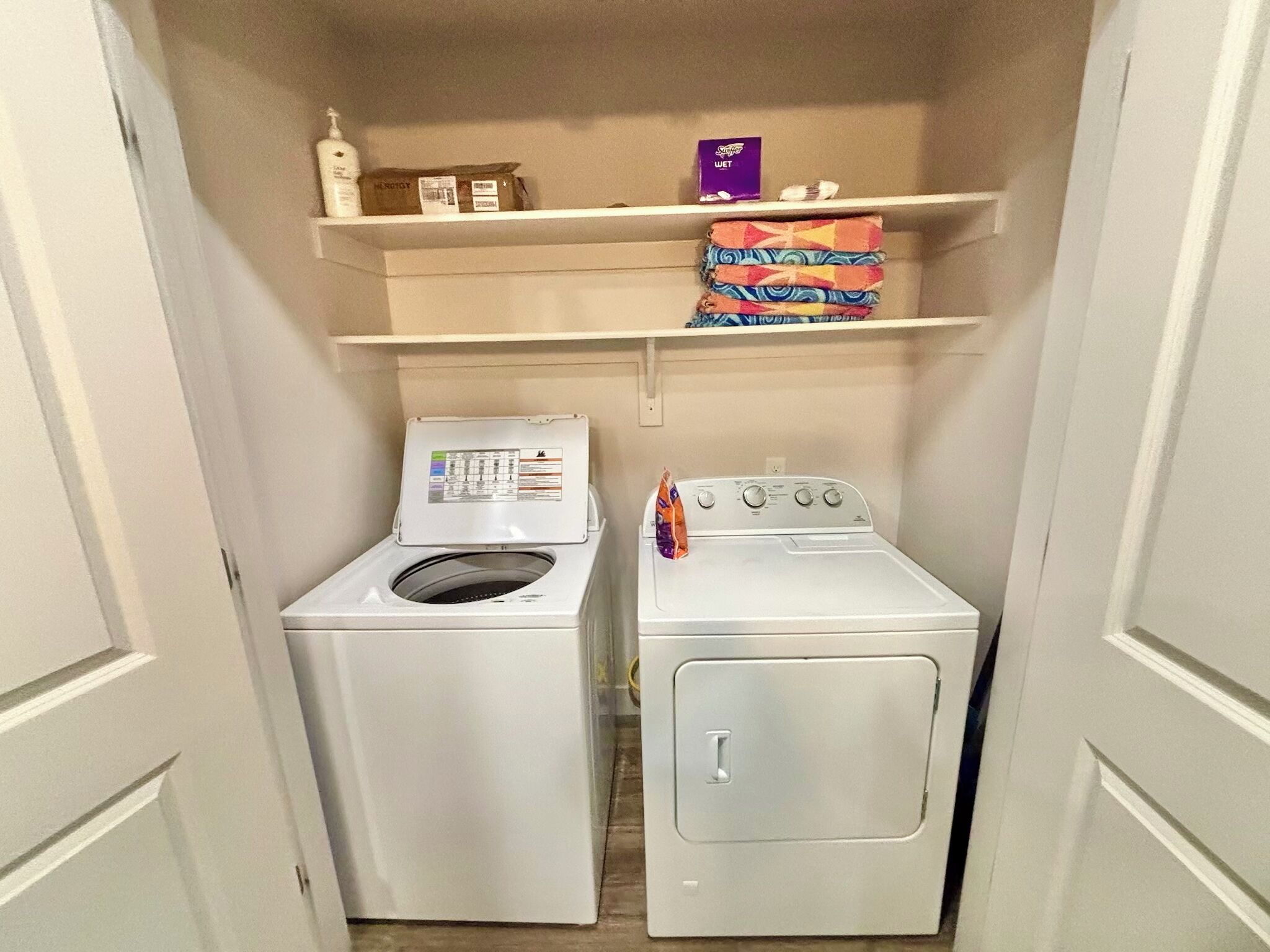 A laundry room with a front-loading washer and dryer, a shelf above the dryer with a box of detergent and a small item.