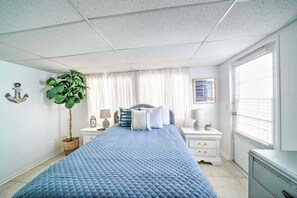 Et soveværelse med seng, natborde, lampe, en plante og et vindue med persienner.