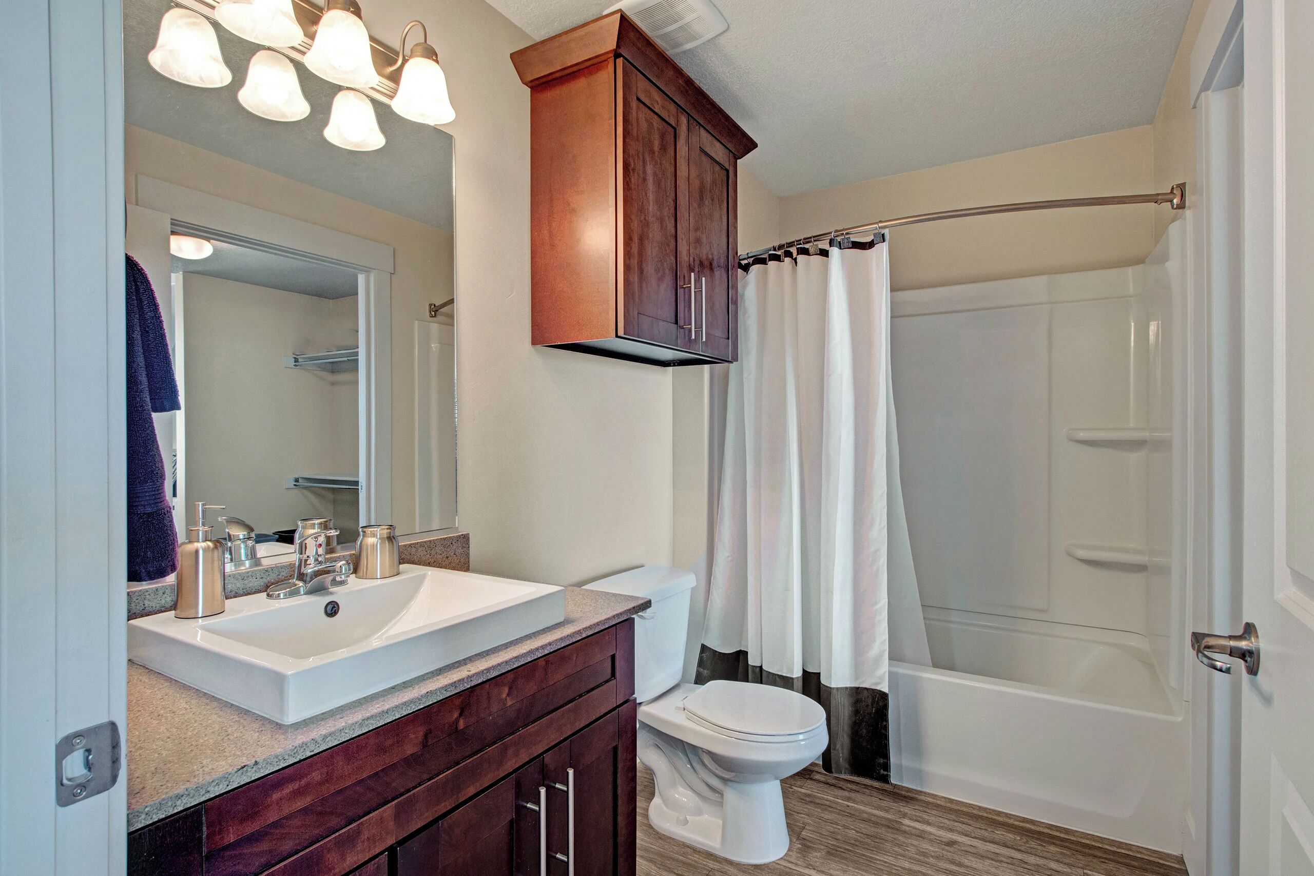 A bathroom with a white sink, dark wooden vanity, a mirror, a white toilet, and a shower with a curtain.