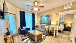 A well-lit living room with a ceiling fan, a sofa, a coffee table, and a TV. - Spacious 2-Bedroom Urban Oasis (Salt Lake City)