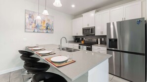 A modern kitchen with white cabinets, stainless steel appliances, and pendant lighting. - Magical Retreat at Championsgate (Davenport)
