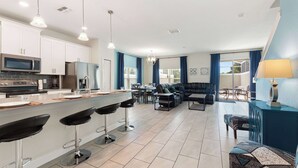 A modern kitchen with a central island, bar stools, and a dining area with a sofa and table. - Magical Retreat at Championsgate (Davenport)