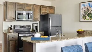 A modern kitchen with a central island, stainless steel appliances, wooden cabinets, and a blue chair. - Charming 1-bedroom villa with AC in fantastic San Antonio (San Antonio)