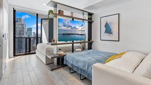 A modern bedroom with a large TV, a bed, a sofa, and a balcony with a city view. - New Open Concept Studio | Walk to Bayfront Park (Miami)