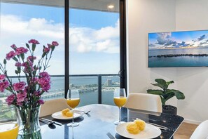 Une table à manger avec vue sur la ville et l’eau, un vase de fleurs et un tableau accroché au mur.