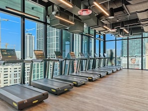 A gym with treadmills aligned against a large window overlooking a cityscape. - World Cup Hub | 2BR Suite | Downtown Miami (Miami)