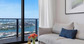 A modern living room with a large window overlooking a cityscape and water. - World Cup Hub | 2BR Suite | Downtown Miami (Miami)