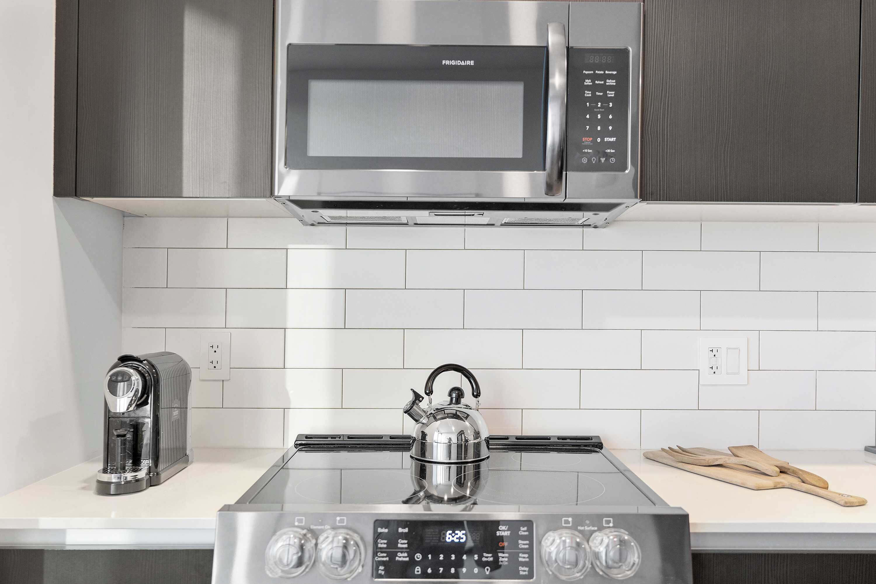 A kitchen with a stainless steel microwave, a coffee maker, and a kettle on a glass-top stove.