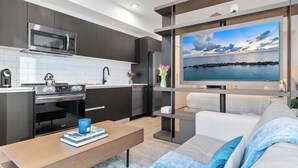 A modern kitchen with dark cabinets, a microwave, and a large flat-screen TV displaying a scenic view. - Floor-to-Ceiling Views | Downtown Studio Suite (Miami)