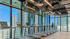Une salle de sport avec des tapis de course alignés le long d’une grande baie vitrée donnant sur un paysage urbain.