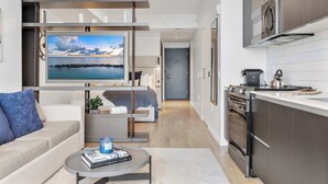 Un salon moderne doté d’un grand téléviseur, d’un canapé, d’une table basse et d’une cuisine équipée d’une cuisinière et d’un four.